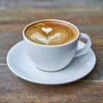 Foto von einer weißen Kaffeetasse mit einem Herzchen im Kaffee.